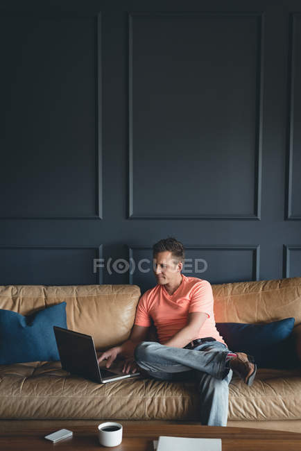 Бизнесмен, использующий ноутбук на диване в офисе — стоковое фото