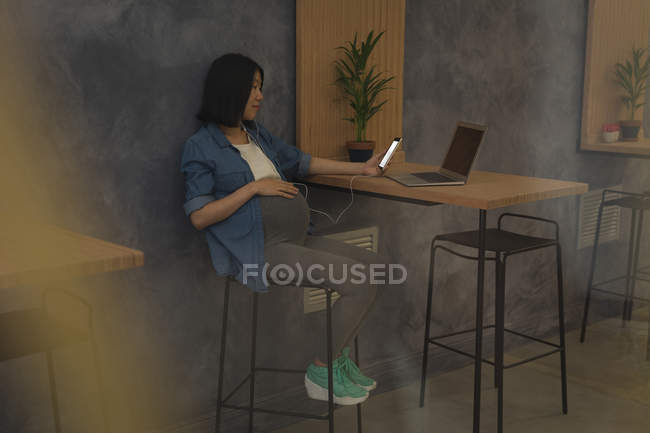 Embarazada mujer de negocios utilizando el teléfono móvil en el escritorio en la oficina - foto de stock