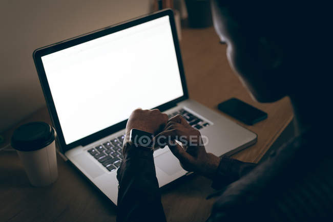Ejecutiva femenina usando smartwatch mientras trabaja en la computadora portátil en el escritorio en la oficina - foto de stock