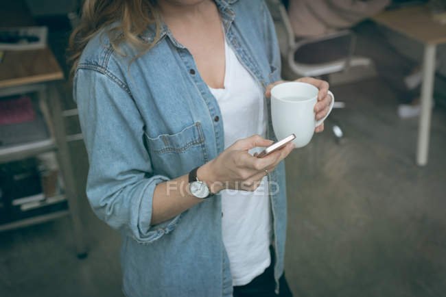 Femme exécutive utilisant un téléphone portable tout en prenant un café au bureau — Photo de stock