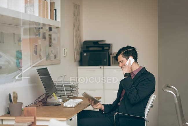Чоловік-виконавчий виступає на мобільному телефоні, тримаючи цифровий планшет в офісі — стокове фото