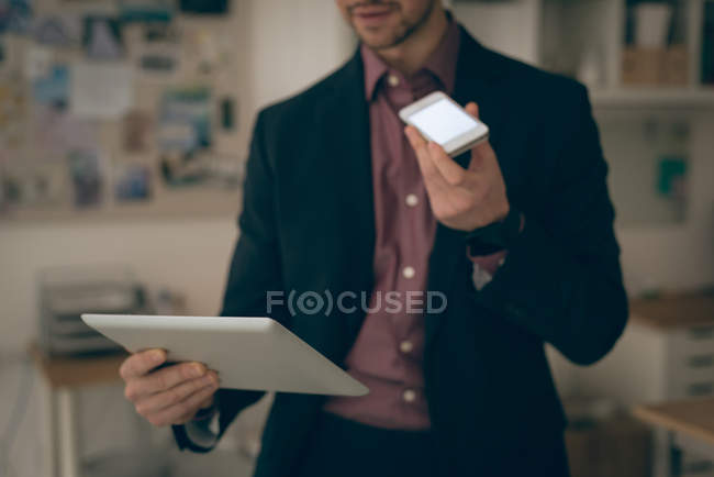 Male executive talking on mobile phone while holding digital tablet in office — Stock Photo