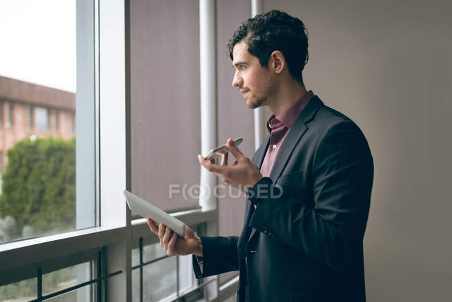 Male executive talking on mobile phone while holding digital tablet in office — Stock Photo