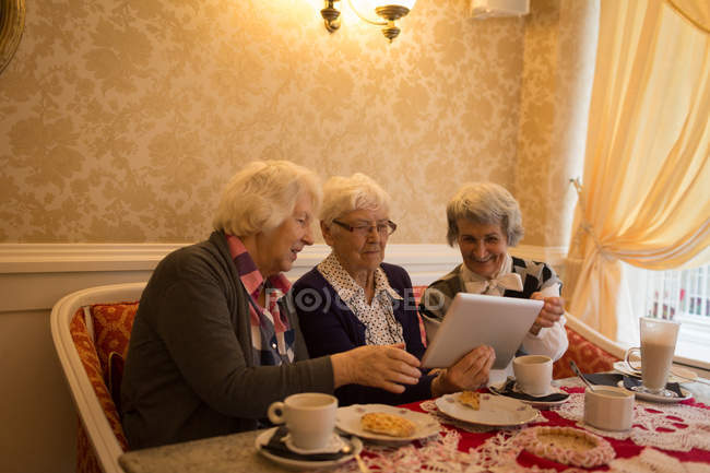 Amigos mayores usando tableta digital mientras desayunan en casa - foto de stock