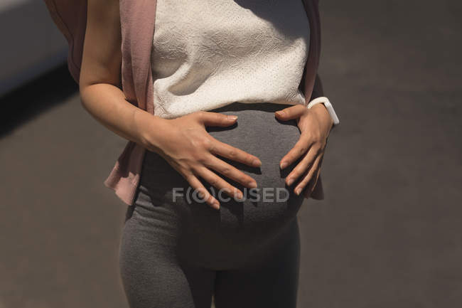 Mittelteil einer Schwangeren, die an einem sonnigen Tag ihren Bauch berührt — Stockfoto