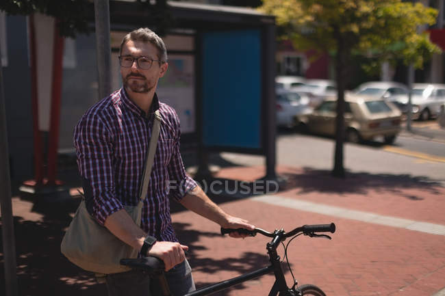 Homme avec vélo debout dans la rue par une journée ensoleillée — Photo de stock