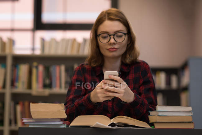 Молода жінка використовує смартфон у бібліотеці — стокове фото