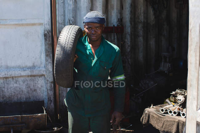 Portrait of mechanic carrying tyre in garage — Stock Photo