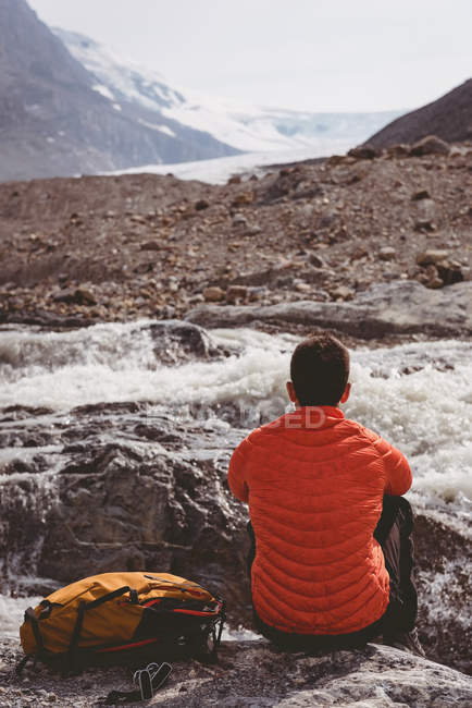 Вид сзади на самца туриста с рюкзаком, отдыхающего у реки — стоковое фото