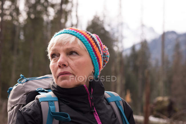 Продумана старша жінка стоїть з рюкзаком взимку — стокове фото