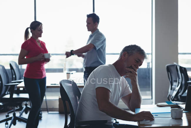 Geschäftsmann arbeitet, während Kollegen im Büro miteinander interagieren — Stockfoto