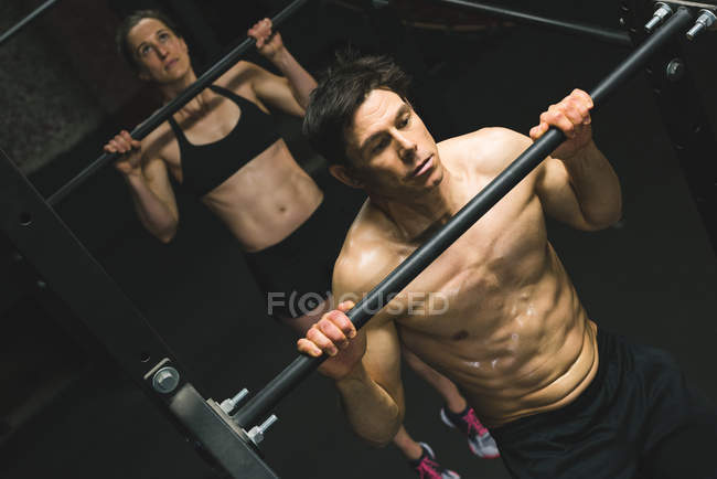 Casal muscular praticando puxar para cima em um bar puxar para cima no ginásio — Fotografia de Stock