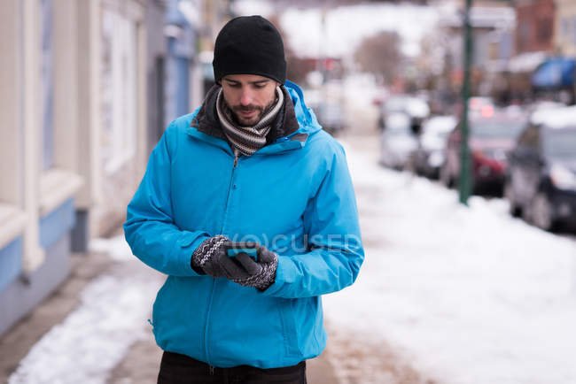 Homem usando telefone celular enquanto caminha na calçada durante o inverno — Fotografia de Stock