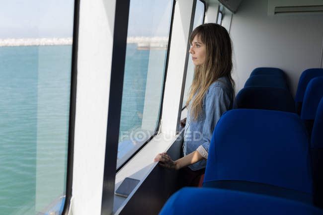 Schöne Frau beim Segeln im Kreuzfahrtschiff durch das Fenster — Stockfoto
