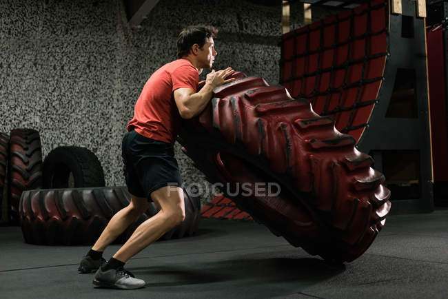 Uomo muscolare ribaltamento pneumatico in palestra — Foto stock
