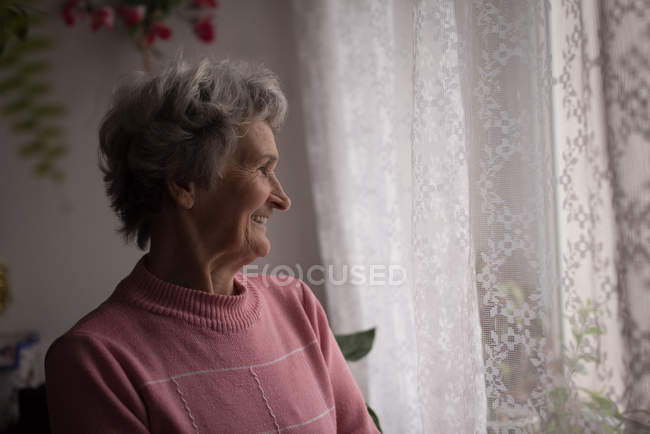 Femme âgée réfléchie souriant à la maison — Photo de stock