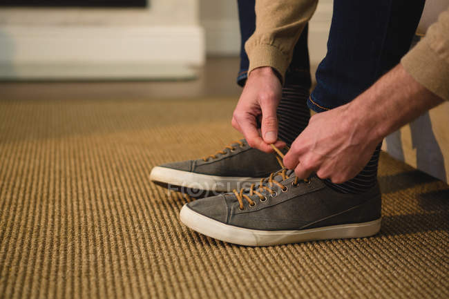 Низька частина людини, що зв'язує шнурки у вітальні вдома — стокове фото
