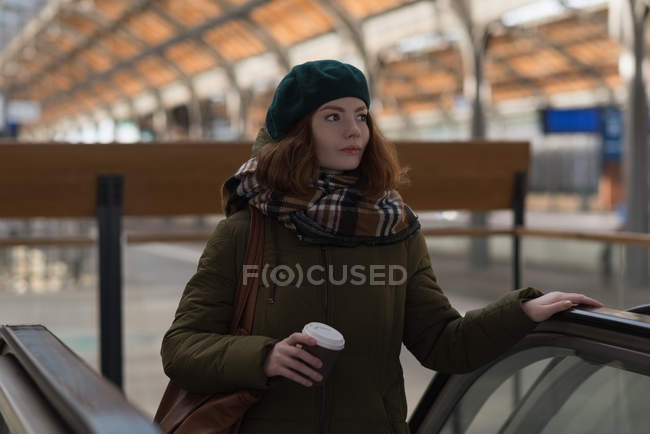 Жінка тримає чашку кави на ескалаторі на залізничній станції — стокове фото