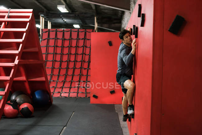 Man practicing rock-climbing on a wall in fitness studio — Stock Photo