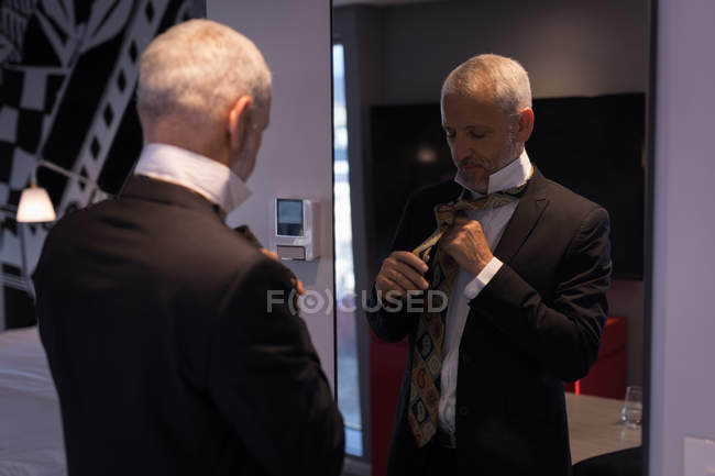 Empresário amarrando um laço na frente de um espelho no quarto de hotel — Fotografia de Stock