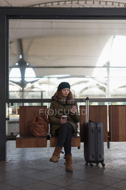 Mulher com xícara de café usando telefone celular na área de espera — Fotografia de Stock