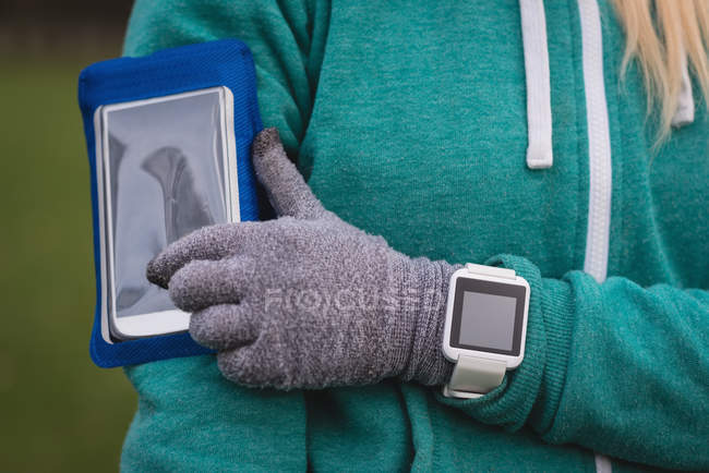 Средняя секция женщины, использующей мобильный телефон с браслетом в парке — стоковое фото