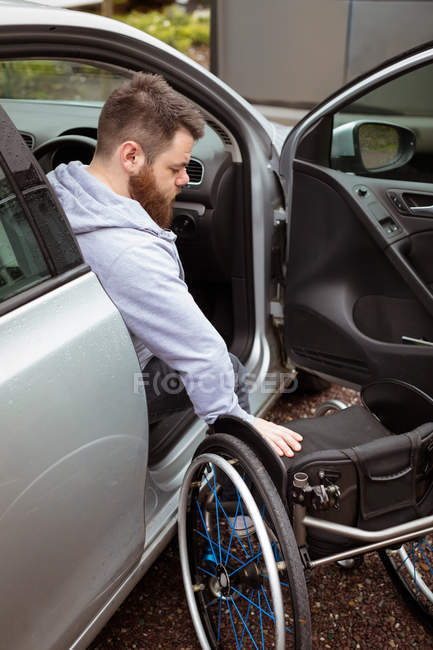 Jovem deficiente segurando cadeira de rodas enquanto embarca em seu carro — Fotografia de Stock