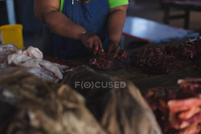 Sección media del carnicero cortando carne en el mostrador en la carnicería - foto de stock