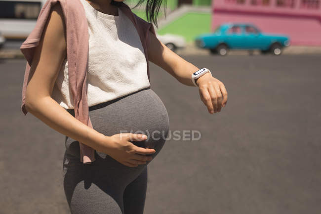 Femme enceinte vérifiant l'heure sur sa montre par une journée ensoleillée — Photo de stock