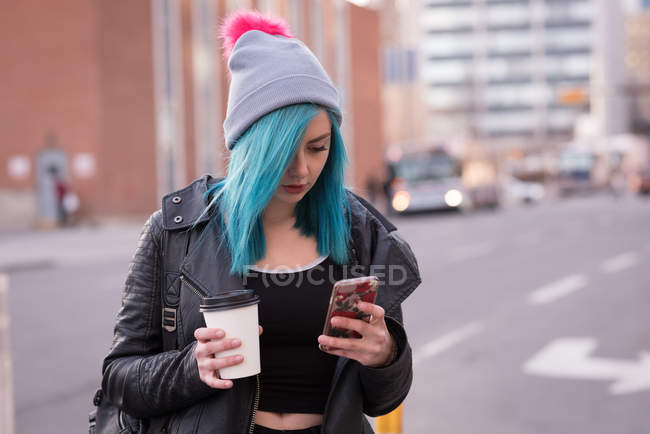 Mulher elegante usando telefone celular enquanto toma café na rua da cidade — Fotografia de Stock