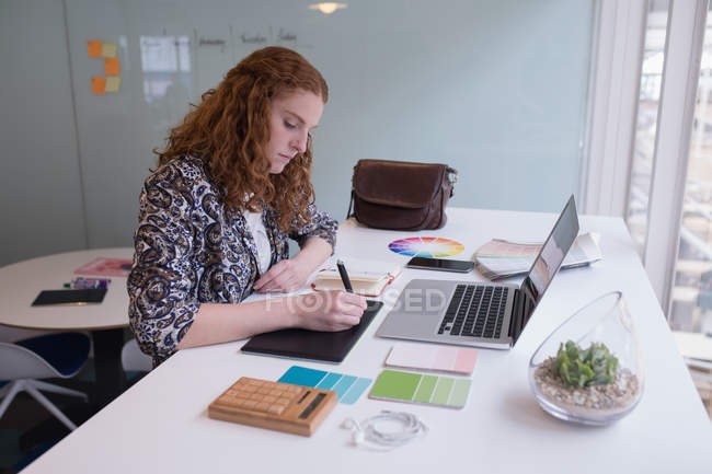 Жіночий графічний дизайнер, використовуючи графічний планшет за столом в офісі — стокове фото