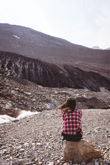 Vista posteriore della donna seduta sulla roccia vicino al fiume — Foto stock