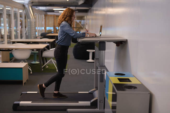 Женщина-руководитель с помощью ноутбука на беговой дорожке в офисе — стоковое фото