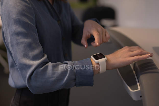 Sección media del ejecutivo femenino usando smartwatch en la cinta de correr en la oficina - foto de stock