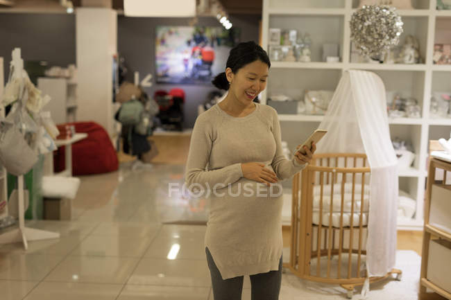 Счастливая беременная женщина с помощью мобильного телефона в магазине — стоковое фото