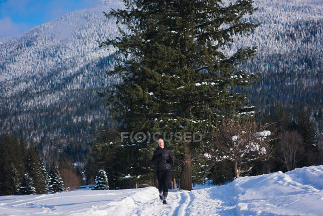 Femme athlétique jogging sur un paysage enneigé par une journée ensoleillée — Photo de stock