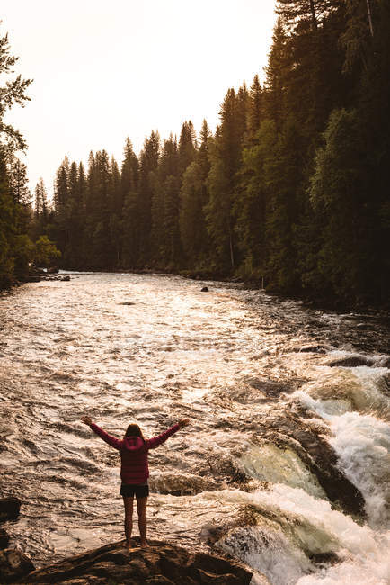 Vista posteriore della donna in piedi con le braccia tese vicino alla cascata — Foto stock