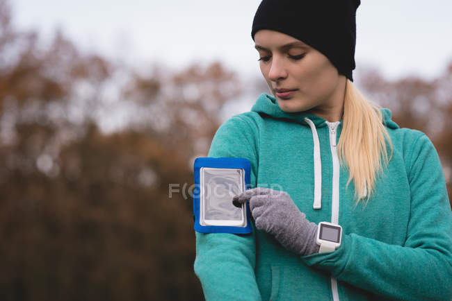 Jovem usando telefone celular com braçadeira no parque — Fotografia de Stock