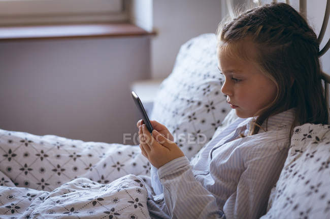 Menina bonito usando telefone celular na cama em casa — Fotografia de Stock