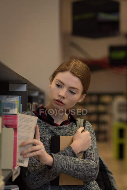 Giovane donna che prende un libro dalla libreria in biblioteca — Foto stock