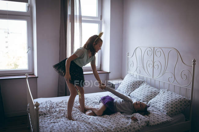 Sorellina in costume che gioca sul letto in camera da letto — Foto stock