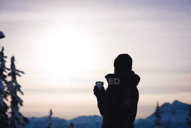 Mulher com café olhando para montanhas cobertas de neve ao entardecer — Fotografia de Stock