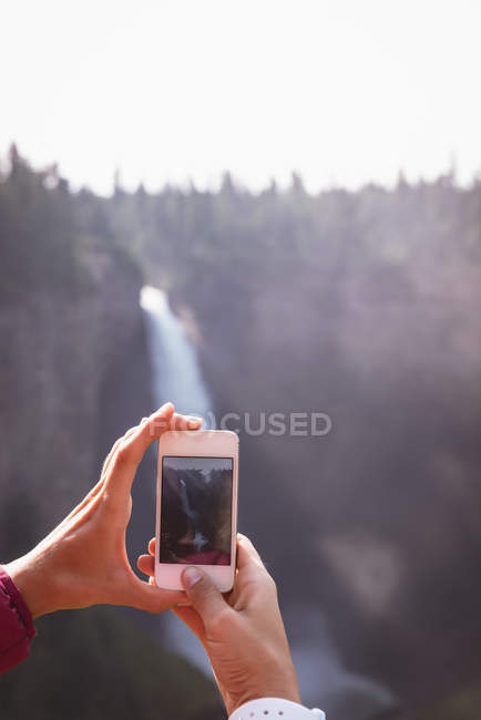 Woman taking photo of waterfall with mobile phone on a sunny day — Stock Photo