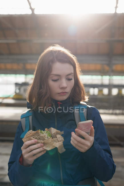 Жінка, використовуючи мобільний телефон, під час обгортання їжі на залізничній станції — стокове фото