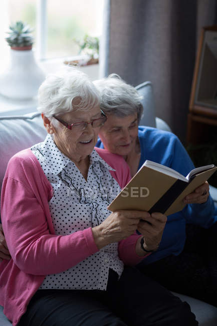 Amis aînés lisant un livre ensemble à la maison — Photo de stock