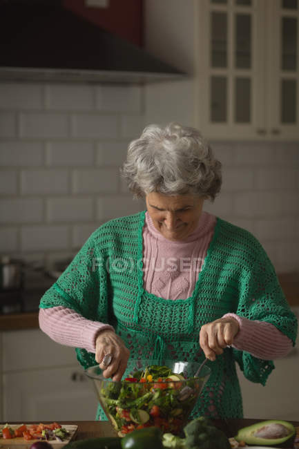 Mulher sênior preparando salada de legumes na cozinha em casa — Fotografia de Stock