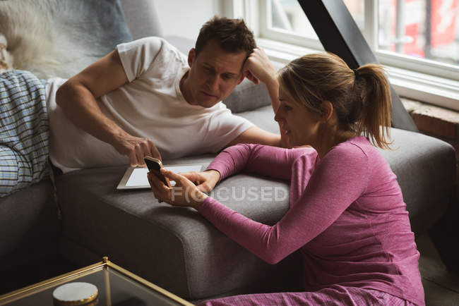 Couple using mobile phone in living room at home — Stock Photo
