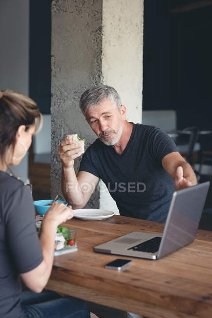 Деловые коллеги обсуждают за ноутбуком за завтраком в офисе — стоковое фото