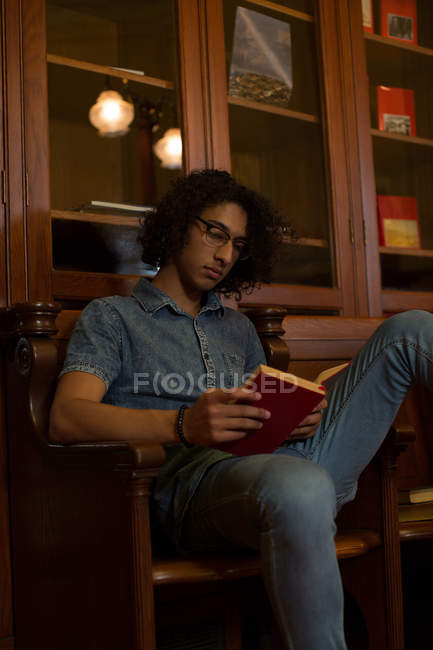 Junger Mann liest in Bibliothek ein Buch — Stockfoto