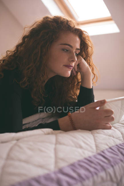 Жінка використовує цифровий планшет, лежачи на ліжку в спальні вдома — стокове фото